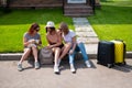 Three Caucasian women and a dog go on a trip. The girls are sitting on the curb with suitcases and waiting for a taxi Royalty Free Stock Photo