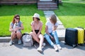 Three Caucasian women and a dog go on a trip. The girls are sitting on the curb with suitcases and waiting for a taxi Royalty Free Stock Photo