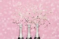 Three Champagne bottles with confetti stars on pink background. Copy space, top view