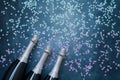 Three Champagne bottles with holographic confetti stars on blue background. Copy space, top view