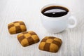 Three checkered shortbread cookies, cup of coffee on table