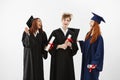 Three cheerful graduates smiling speaking fooling holding diplomas over white background.