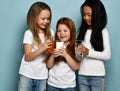 Three joyful kids girls friends in white t-shirts share their favorite drinks water, milk and juice toasting celebrating