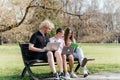 Three cheerful students study and work together outdoors on a sunny day, using laptops and notebooks while sitting on a Royalty Free Stock Photo