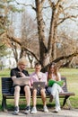 Three cheerful students study and work together outdoors on a sunny day, using laptops and notebooks while sitting on a Royalty Free Stock Photo