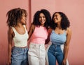 Three cheerful women with curly hair having fun together while standing at a pink wall Royalty Free Stock Photo