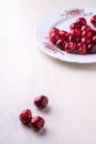 Three cherry berries with white plate with cherries in background on wooden white background angle view Royalty Free Stock Photo
