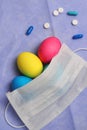 Three chicken easter eggs colored blue pink yellow colors covered white medical mask and  medicine pills scattered around Royalty Free Stock Photo