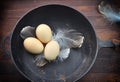 Three chicken eggs in a shell in a black cast-iron frying pan,