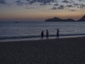 Three childern playing on sea shore Agios Georgios Pagon beach at Corfu island, Greece at blue hour after pink orange sunset with
