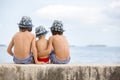 Three children, boy brothers, sitting on a concrete wall on pier on the sea, contemplating the boats Royalty Free Stock Photo