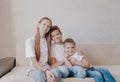 Three children, a girl and two boys in white T-shirts and blue jeans, sit hugging each other on the home sofa and smile Royalty Free Stock Photo