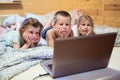 Three children looking at laptop while are in bed