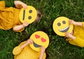 Three children lying on the grass are holding cardboard emoticons Royalty Free Stock Photo