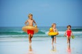 Three children run with inflatable buoys doughnut, duck on beach Royalty Free Stock Photo