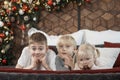 Three children siblings on bed on Christmas decorations background. Two older brothers and little sister in bedroom Royalty Free Stock Photo