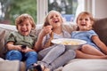 Three Children Sitting On Sofa At Home Laughing And Watching TV With Popcorn Royalty Free Stock Photo