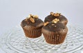 Three chocolate brown muffins with nuts on glass plate detail