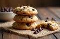 Three chocolate chip cookies stacked on burlap. One cookie broken, showing chips inside. Choc chips scatter around and in bowl. Royalty Free Stock Photo