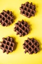 Three chocolate waffles on a yellow background, flat lay, top view