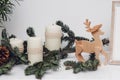 Three Christmas candles, pinecone, baubles, branch of pine, gsarland and wooden deer on the white table. Celebration and Royalty Free Stock Photo