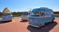 Three Classic Volkswagen Camper Van parked together with beach huts in the background.