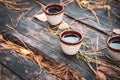 Three clay cup with liqueur on wooden table, outdoor. Table with needles and leaf and ceramic small coffee mugs. Picnic concept. Royalty Free Stock Photo