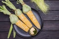 Three cobs of fresh corn and bowl of sauce on black plate