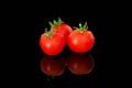 Three coctail tomatoes sprinkled with water on black reflective surface