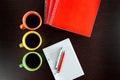 Three coffee cups stay on dark brown wooden table like lights beside the sketchbook with orange notebooks and orange and white pe Royalty Free Stock Photo