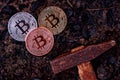 Three coins of bitcoin on black earth and a hammer