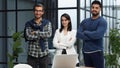 three colleagues stand in the lobby of a modern office with their arms crossed