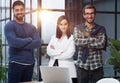 three colleagues stand in the lobby of a modern office with their arms crossed