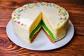 Three-color cake on a wooden table. A plate of dessert with layers of green, brown and white. Sprinkled with candy and soaked with