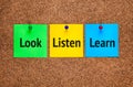 Three colored notes on corkboard with words Look, Listen, Learn
