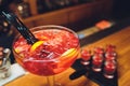 Three colorful cocktails in large glasses in a classic bar environment with dozens of blurry liquor bottles in the