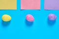 Three colorful eggs with glitters near blank square paper stickers lies on blue desk on kitchen Royalty Free Stock Photo