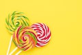 Three colorful lollipops on a white stick on a bright yellow background. Top view, copy space Royalty Free Stock Photo