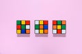 Three colorful Rubiks cubes on a pink background