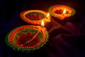 Three colorful terracotta oil lamp or diya lit during diwali on blue cloth background