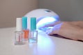 Three colorless transparent nail polish bottles in background of female hands in gel uv led nail white lamp for drying manicure Royalty Free Stock Photo