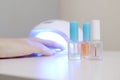 Three colorless transparent nail polish bottles in background of female hands in gel uv led nail white lamp for drying manicure Royalty Free Stock Photo