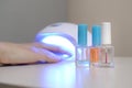 Three colorless transparent nail polish bottles in background of female hands in gel uv led nail white lamp for drying manicure Royalty Free Stock Photo