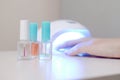 Three colorless transparent nail polish bottles in background of female hands in gel uv led nail white lamp for drying manicure Royalty Free Stock Photo