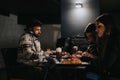 Three concentrated freelancers working on their laptops in a dimly lit cafe at night, surrounded by coffee and pastries.