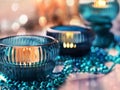 Three cozy lighted candles in turquoise candlesticks with Christmas garland in warm colors with bokeh effect