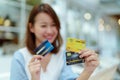 Three credit cards are in the hands of an Asian woman by an out of Focus Asian woman sitting in a bakery preparing for online shop Royalty Free Stock Photo