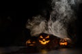 Three creepy Halloween grinning pumpkins glow in the dark among the fog. jack-o-lantern in a witch hat on a black