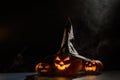 Three creepy Halloween grinning pumpkins glow in the dark among the fog. jack-o-lantern in a witch hat on a black