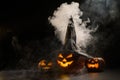 Three creepy Halloween grinning pumpkins glow in the dark among the fog. jack-o-lantern in a witch hat on a black